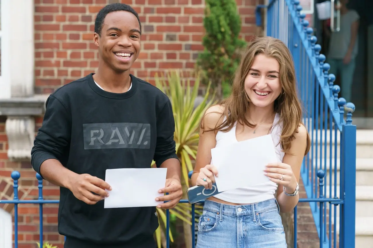 Two smiling students, a young man and a young woman, proudly holding up their exam result papers