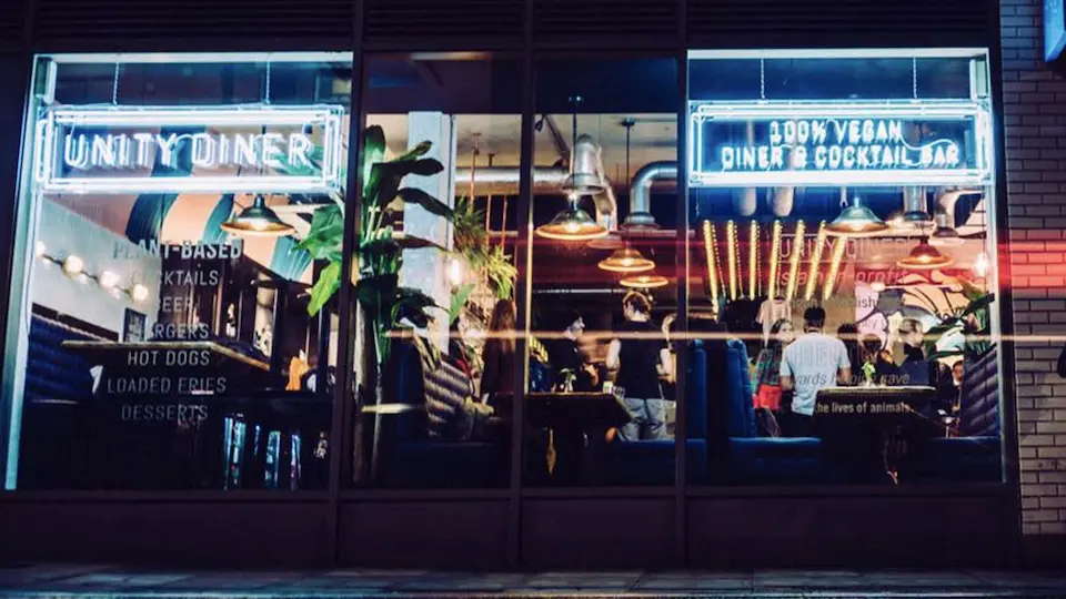 A view through the window of Unity Diner at night, with bright neon signs illuminating the diners inside