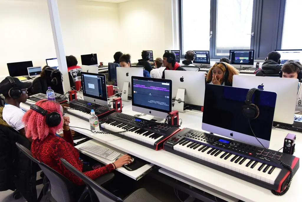Students wearing headphones working on Apple Mac computers with music keyboards in a modern tech lab