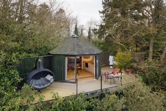 Elevated wooden deck of HappenOak Treehouse showing a hanging egg chair and outdoor seating, surrounded by trees