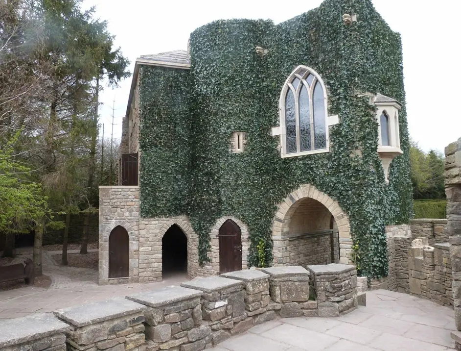 Exterior of a quirky stone folly building at The Forbidden Corner, covered heavily in ivy, with arched doorways